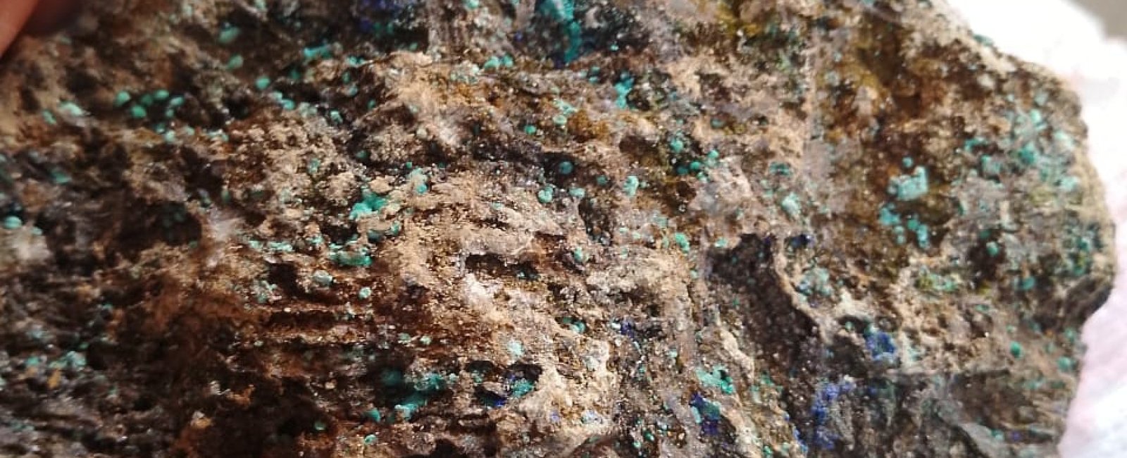 Raw gold ore with visible flecks shown alongside blurred icons of smelting, bullion, and electronics—highlighting real-world gold ore applications.